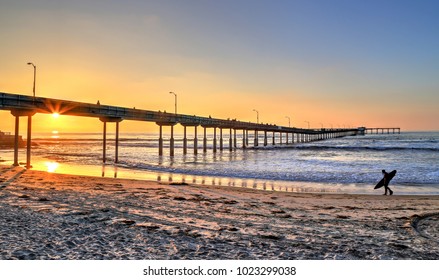 A surfer walks on Ocean Beach near the pier in San Diego, California. - Powered by Shutterstock