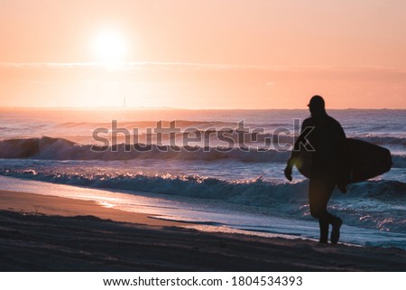 A surfer walks past the sunrise
