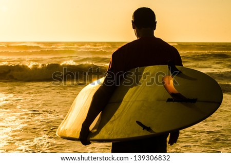 A surfer watching the waves at sunset in Portugal.