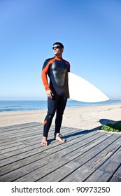 Surfer Wearing A Long Wetsuit Holding His Surf Board.