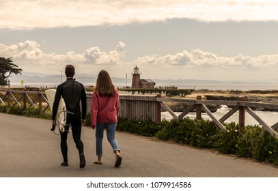 Surfer with a wetsuit and surfboard walking with a friend towards the Santa Cruz Surfing Museum and Lighthouse in springtime. West Cliff Drive, Santa Cruz, Northern California, USA.  - Powered by Shutterstock