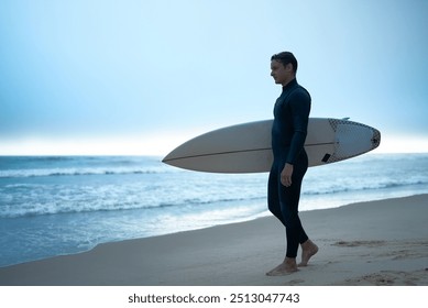 Surfer in wetsuit walking along the beach carrying a surfboard at twilight. Calm ocean waves and serene atmosphere create a peaceful and contemplative scene. - Powered by Shutterstock