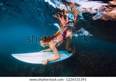 Surfer woman with surf board dive underwater with under big ocean wave