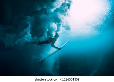Surfer woman with surfboard dive underwater with under big wave.