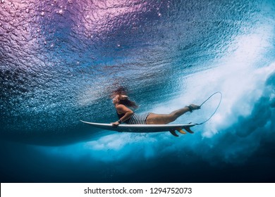 Surfer woman with surfboard dive underwater with under ocean waves.