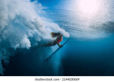 Surfer woman with surfboard dive underwater with under big ocean wave.