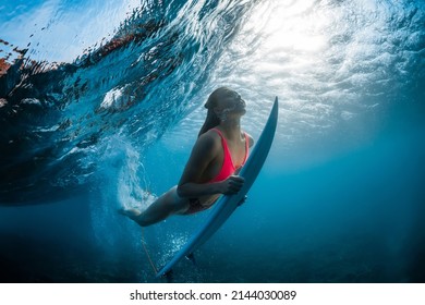 Surfer woman with surfboard dive underwater with under barrel wave and sunlight in transparent ocean.