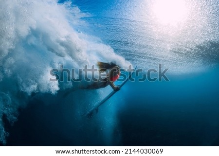 Surfer woman with surfboard dive underwater with under big ocean wave.
