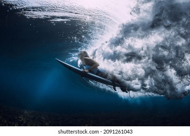 Surfer woman with surfboard duck dive under wave in ocean.