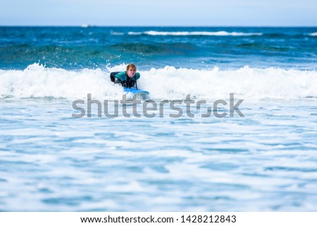 Surfer woman with surfboard is paddling on the wave. Girl in surfing wet suit is paddling the waves of cold atlantic ocean in Galicia, Spain.