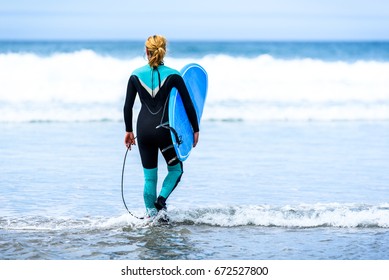 Surfer woman with surfboard is walking and watching the waves. Girl in surfing wet suit is observing the waves of cold atlantic ocean in Galicia, Spain.