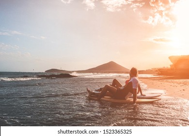 Surfers couple sitting on boards after surfing day on the beach - Tourist having fun traveling during vacation together - Extreme sport, relationship and travel concept - Soft focus on man body - Powered by Shutterstock