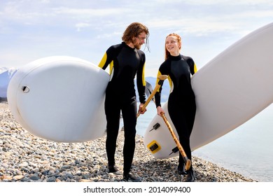 Surfers, Handsome Man And Redhead Woman Walking With Board On Beach, Have Talk. Water Sports. Caucasian Happy Couple Lead Healthy Active Lifestyle. Surfing. Summer Vacation. Extreme Sport. Portrait