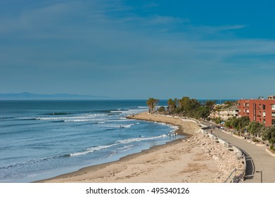 Surfers and pedestrians at Ventura promenade boardwalk along the high tide shore.