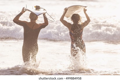 Surfers Running In The Water With Their Boards