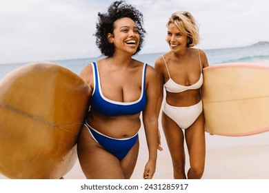 Surfing friends leaving the beach after an exciting coastal adventure, ending a fun vacation with happy memories from riding with the waves. Two female surfers smiling and walking on shore in bikinis. - Powered by Shutterstock