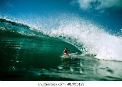 Surfing girl riding a giant ocean wave. Blue ocean water crashing with splashes and drops. Water sport activity 