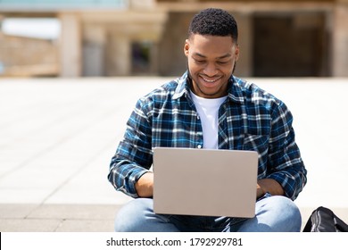 Surfing Internet. Front View Portrait Of Smiling Black Person Typing On Laptop Keyboard, Sitting Outdoor In Park