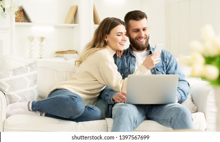 Surfing Internet. Young Couple Relaxing With Laptop And Smartphone, Sitting On Sofa