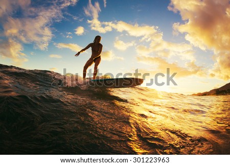 Surfing at Sunset. Beautiful Young Woman Riding Wave at Sunset. Outdoor Active Lifestyle.