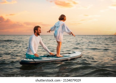 Surfing with sup board. Instructor teaches the pre-school girl to swim with a sup board. Sea and the sunset in the background. Summer vacations.