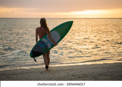 Surfing surfer girl looking at ocean beach sunset. Silhouette of female bikini woman looking at water with standing with surfboard having fun living healthy active lifestyle. Water sports with model.