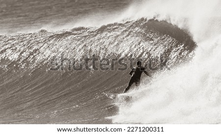 Surfing surfer unrecognizable in hood and wetsuit rear action sepia tone photograph bottom turning rides cold  offshore windy ocean wave