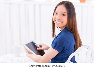 Surfing Web In Cafe. Rear View Of Beautiful Young Asian Woman Using Digital Tablet And Looking Over Shoulder While Sitting In Cafe