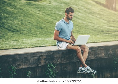 Surfing Web Outdoors. Handsome Young Man In Polo Shirt Working On Laptop While Sitting On Quayside