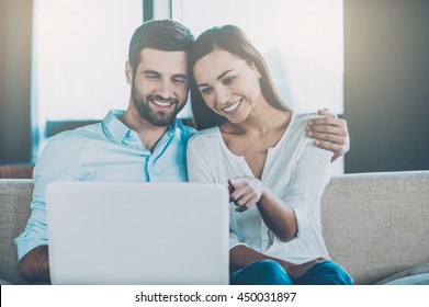 Surfing Web Together. Beautiful Young Loving Couple Sitting Together On The Couch And Looking At Laptop