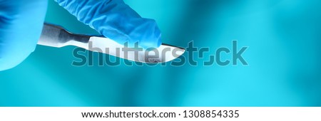 Surgeon arms in sterile uniform holding sharp knife while operating patient in surgical theatre closeup. Stop bleeding put stitch innovation er 911 team cancer tumour concept