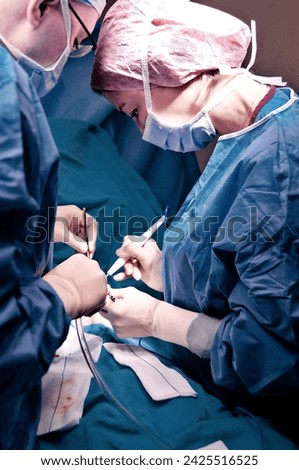 Surgeon and assistant performing cosmetic surgery in hospital operating room. Surgeon in mask wearing loupes during medical procadure. Breast augmentation, enlargement, enhancement, breast cancer