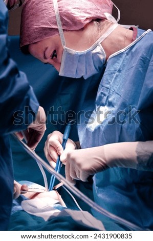 Surgeon and assistant performing cosmetic surgery in hospital operating room. Surgeon in mask wearing loupes during medical procadure. Breast augmentation, enlargement, enhancement, breast cancer