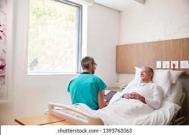 Surgeon With Digital Tablet Visiting Senior Male Patient In Hospital Bed In Geriatric Unit