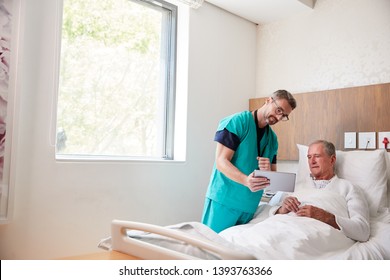 Surgeon With Digital Tablet Visiting Senior Male Patient In Hospital Bed In Geriatric Unit