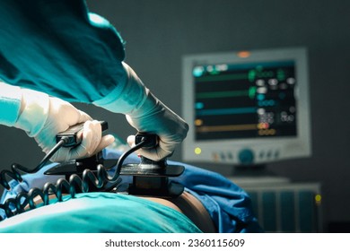Surgeon doctor hand hold defibrillator to pump chest heart patient to save life sick people in operating room at hospital, surgical team using equipment to do surgery. healthcare and medical concept. - Powered by Shutterstock