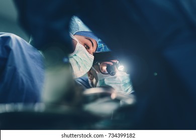 Surgeon doctor operating using special lamp lighting and glasses loupes wearing blue surgical mask and surgical cap in surgery room with his team surgeons operating live heart beating heart surgery
