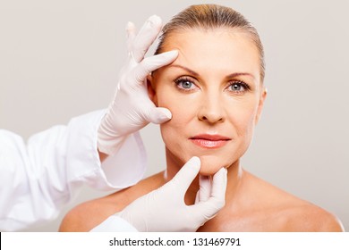 surgeon doing skin check on mid age woman before plastic surgery