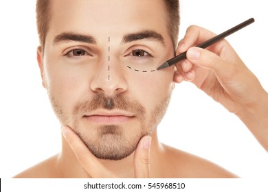 Surgeon Drawing Marks On Male Face Against White Background. Plastic Surgery Concept