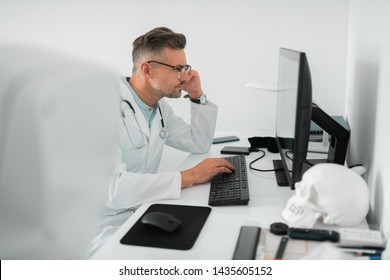 Surgeon Feeling Busy. Professional Handsome Plastic Surgeon Feeling Busy While Working On Computer