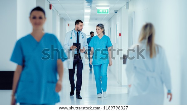 Surgeon\
and Female Doctor Walk Through Hospital Hallway, They Consult\
Digital Tablet Computer while Talking about Patient\'s Health.\
Modern Bright Hospital with Professional\
Staff.