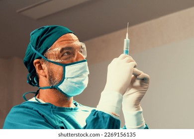 Surgeon fill syringe from medical vial for surgical procedure at sterile operation room. Doctor in full protective wear for surgery prepare anesthesia injection for his patient - Powered by Shutterstock