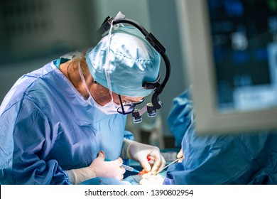 Surgeon and his assistant performing cosmetic surgery in hospital operating room. Surgeon in mask wearing loupes during medical procadure. - Shutterstock ID 1390802954