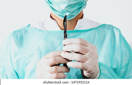 Surgeon holds scalpel dressed in a green surgical apron and mask on light background. Medical and pharmaceutical concept. Scalpel surgeon's scissors, just before surgery. Responsible work of surgeon.