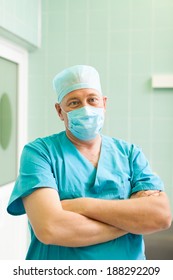 Surgeon Man Relaxed Smile Confident In Surgical Room Hospital, Medical Doctor Wear Green Surgery Scrub Suit, Mask And Cap In Operating