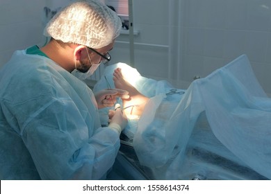 Surgeon man sutures ankle during surgery with neat stitches after removing hygroma. Doctor sewing on wound in operating room in hospital. Seams with self-absorbable threads. One day surgery concept.