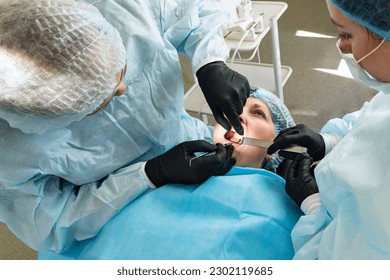 Surgeon and nurse during dental operation. Local anesthetized female patient in surgical room of dental clinic. Installation of dental implants or tooth extraction. 