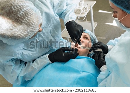 Surgeon and nurse during dental operation. Local anesthetized female patient in surgical room of dental clinic. Installation of dental implants or tooth extraction. 