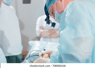 Surgeon performing cosmetic surgery on nose in hospital operating room. Surgeon in mask wearing surgical loupes during medical procedure.