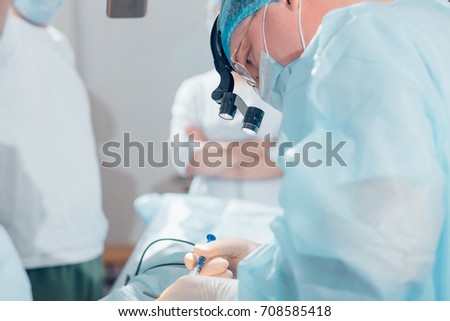 Surgeon performing cosmetic surgery on nose in hospital operating room. Surgeon in mask wearing surgical loupes during medical procedure.